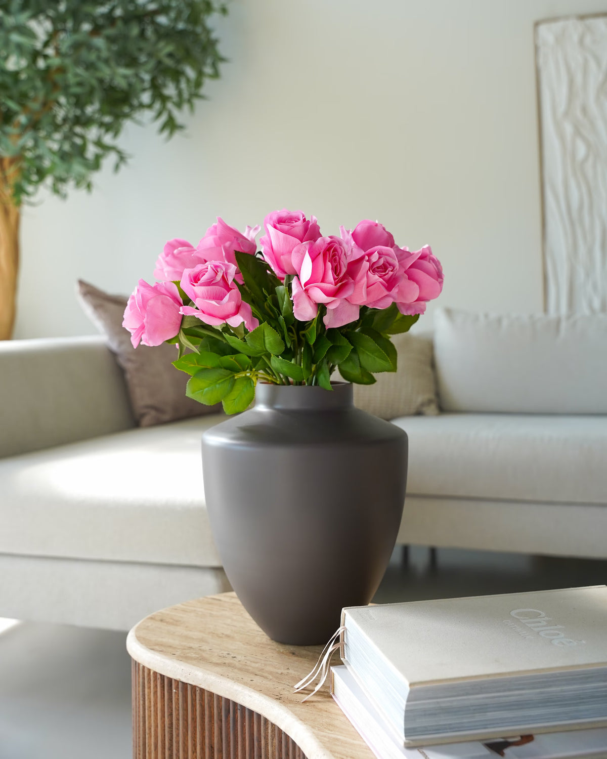 Vaas Tierra S met roze zijden rozen op een ronde houten salontafel voor een lichte hoekbank.