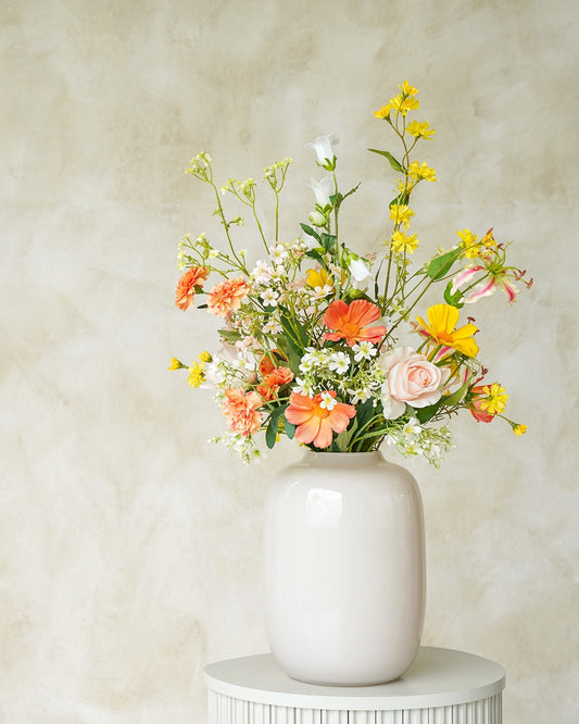 Sfeervol geel met oranje zijden boeket Fio uit de collectie van Fan of Flowers gepresenteerd in vaas Crema.
