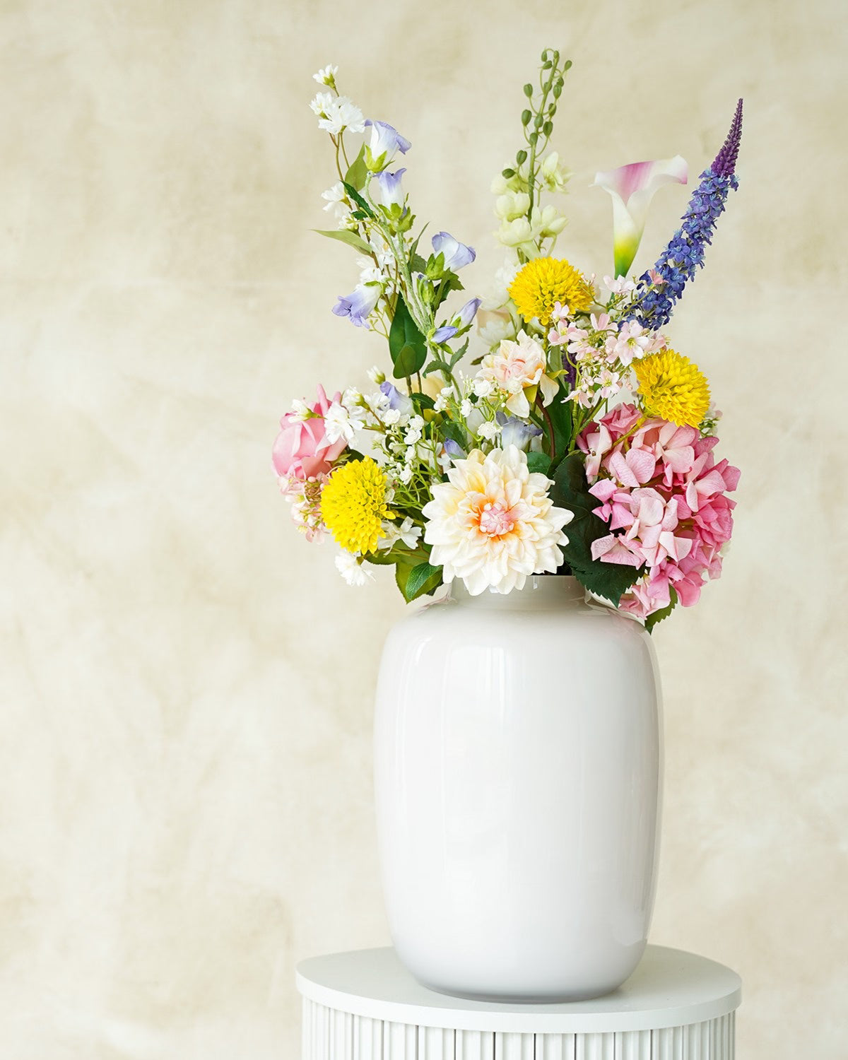 Zomerse kunstbloemen boeket Bella van Fan of Flowers opgesteld in een glanzende crème vaas Crema.