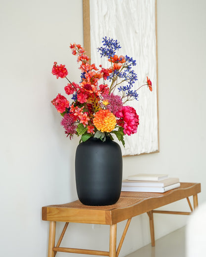Kleurrijk zijden boeket Cielo van Fan of Flowers in matzwarte vaas Negro gestyled op een houten bankje in een modern interieur.
