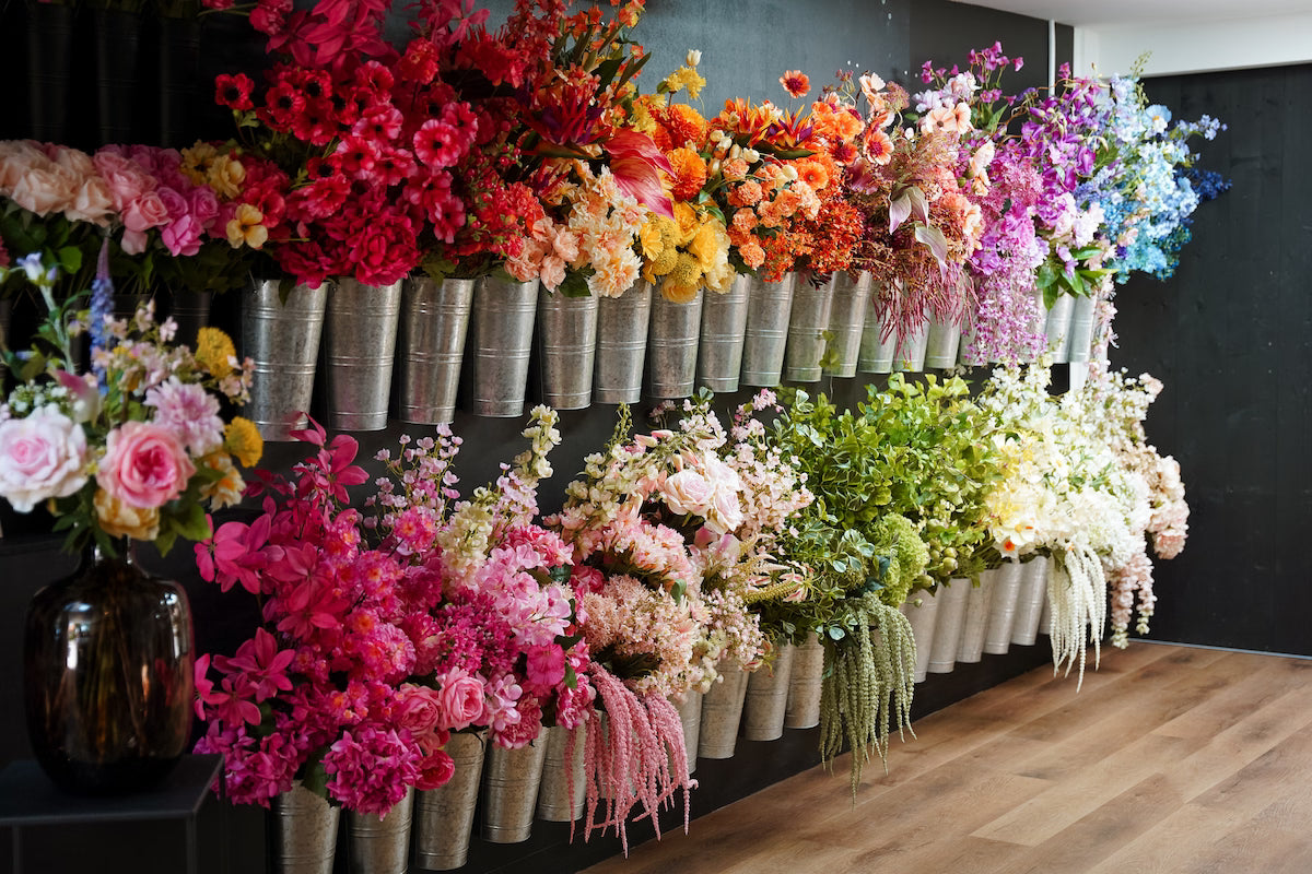 Overzicht van de uitgebreide collectie en voorraad levensechte losse zijden bloemen in zinken emmers aan de muur.