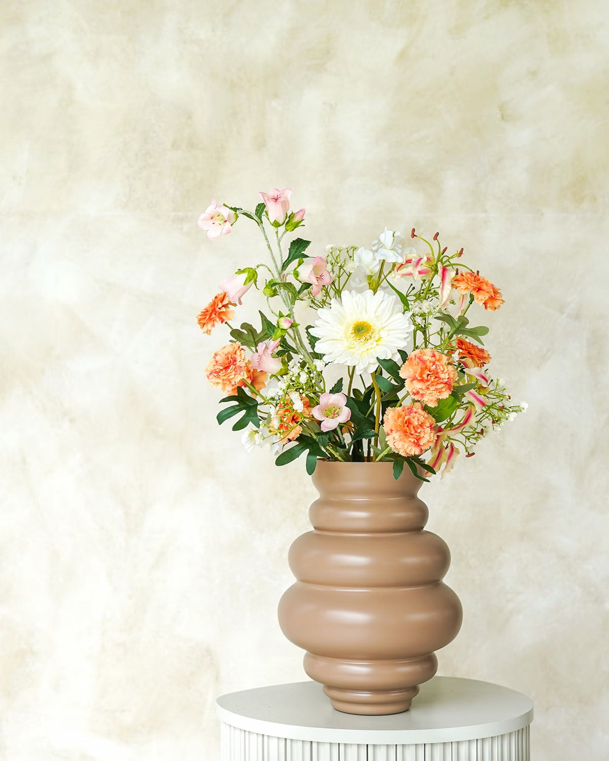 Een matbruine/terracotta Vaas Bomba van Fan of Flowers, maat M, gevuld met het warme zijden Boeket Vela (perzik, koraal, crème) op een marmeren sokkel.