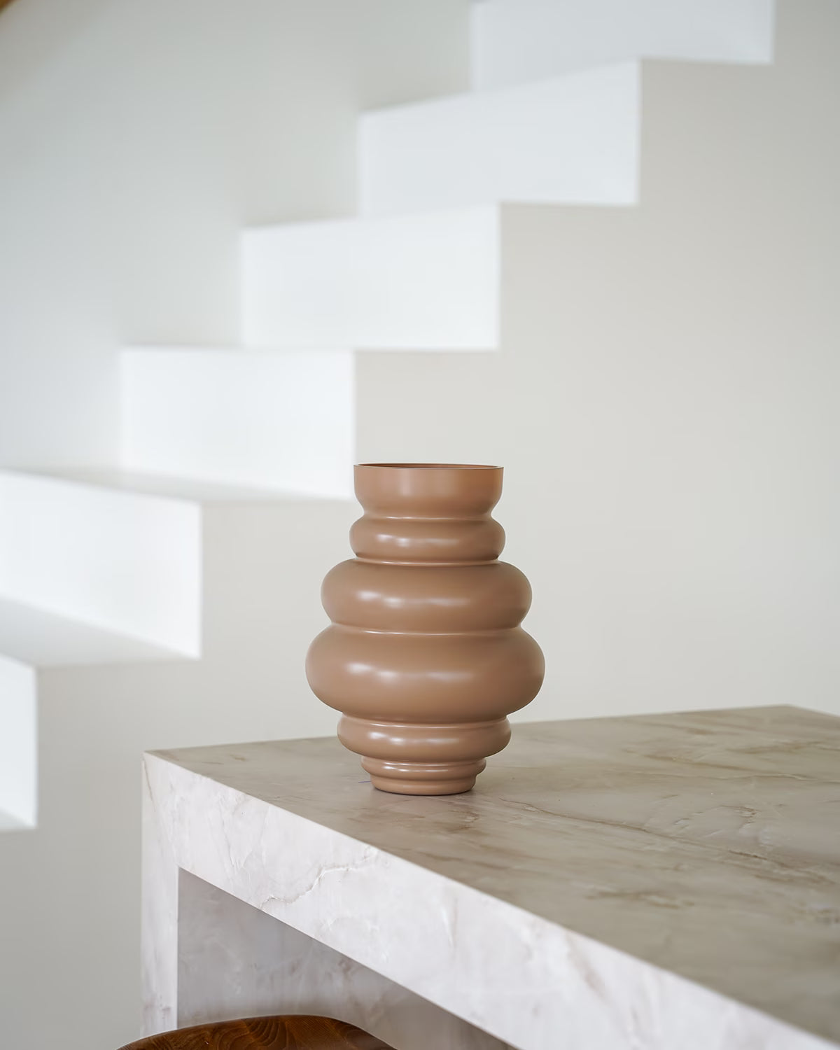 Een lege, matbruine/terracotta Vaas Bomba van Fan of Flowers, maat M, geplaatst op een marmeren bijzettafel tegen een witte achtergrond.