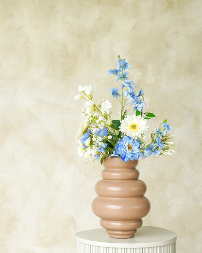 Een matbruine/terracotta Vaas Bomba van Fan of Flowers, maat S, gevuld met het elegante zijden Boeket Celeste (blauw delphinium, witte gerbera) op een marmeren bijzettafel.