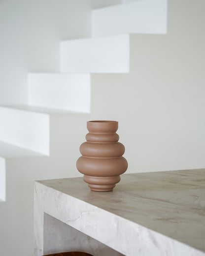 Een lege, matbruine/terracotta Vaas Bomba van Fan of Flowers, maat S, geplaatst op een marmeren bijzettafel tegen een witte achtergrond.