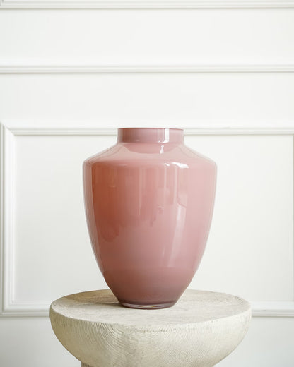 Een lege, glanzende roze vaas Rosa van Fan of Flowers (maat M), geplaatst op een ronde betonnen zuil tegen een achtergrond van klassiek wit lijstwerk.