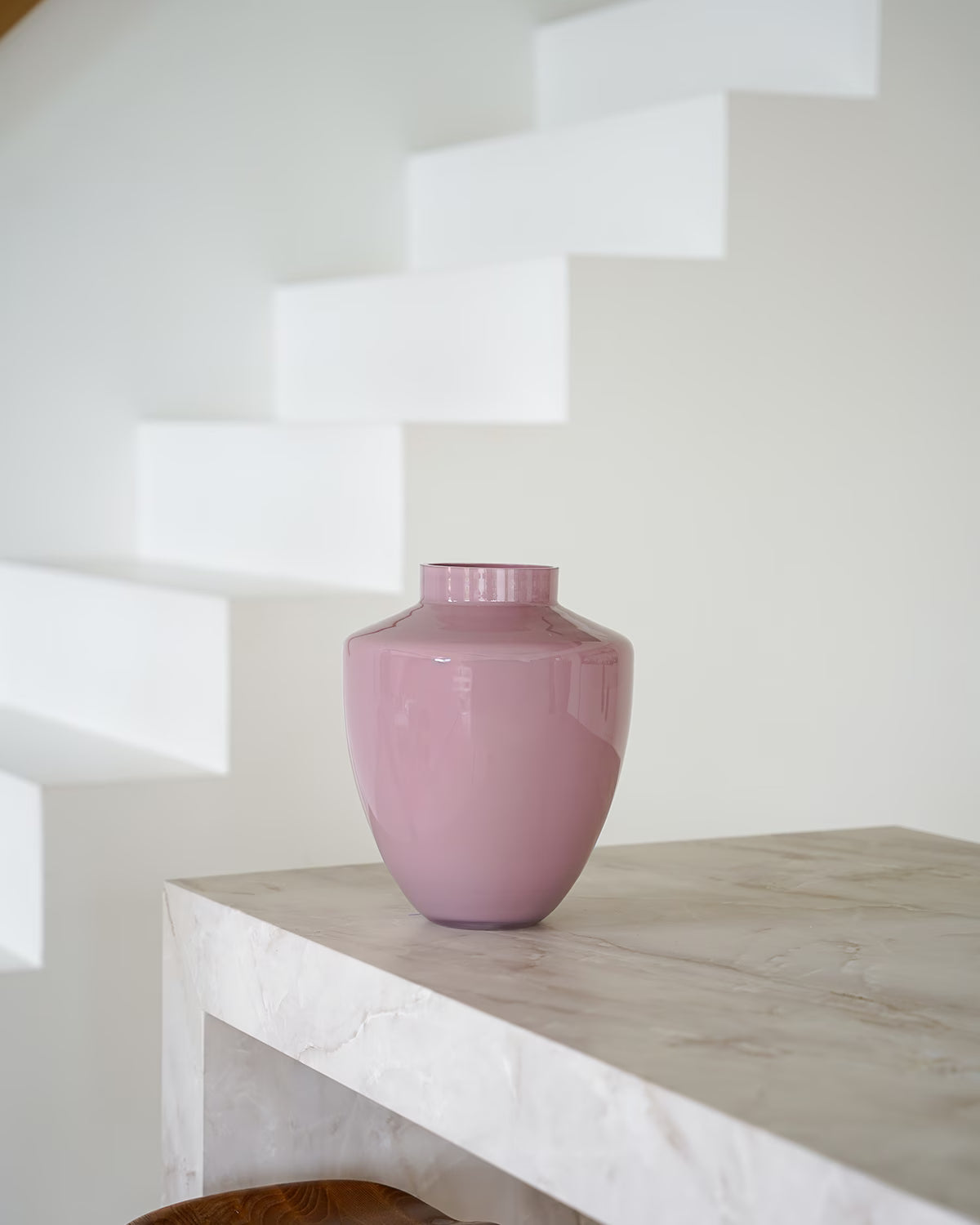 Een lege, glanzend roze vaas Rosa van Fan of Flowers, maat S, geplaatst op een marmeren bijzettafel met een witte achtergrond.