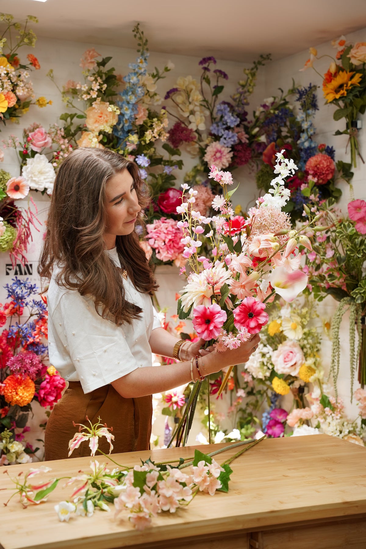 Geconcentreerde Femke Goossens die een roze zijden boeket schikt met losse kunstbloemen op de houten werkbank in het atelier van Fan of Flowers