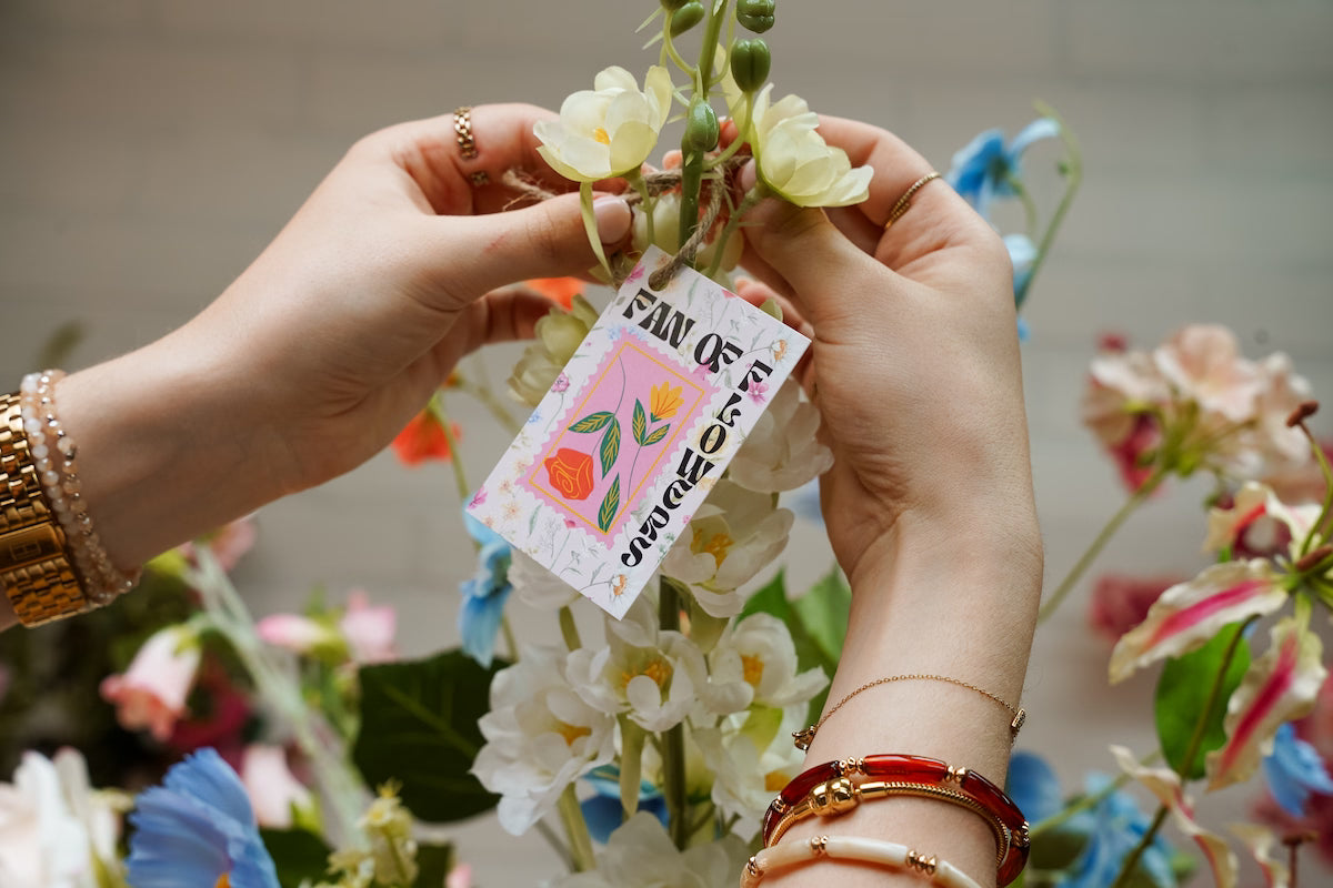 Close-up van de handen van Femke Goossens die een merklabel van Fan of Flowers aan een zijden boeket knoopt.