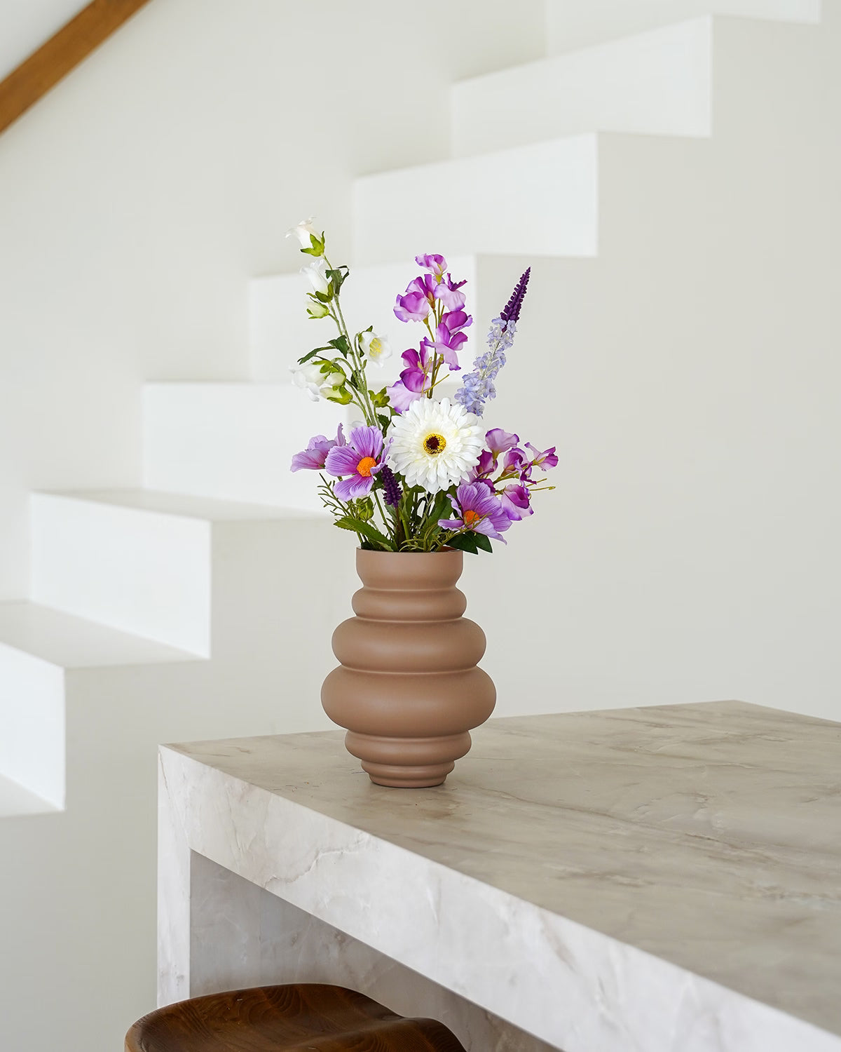 Bruine Vaas Bomba S met het paars-witte zijden boeket Violet van Fan of Flowers op een marmeren tafel.