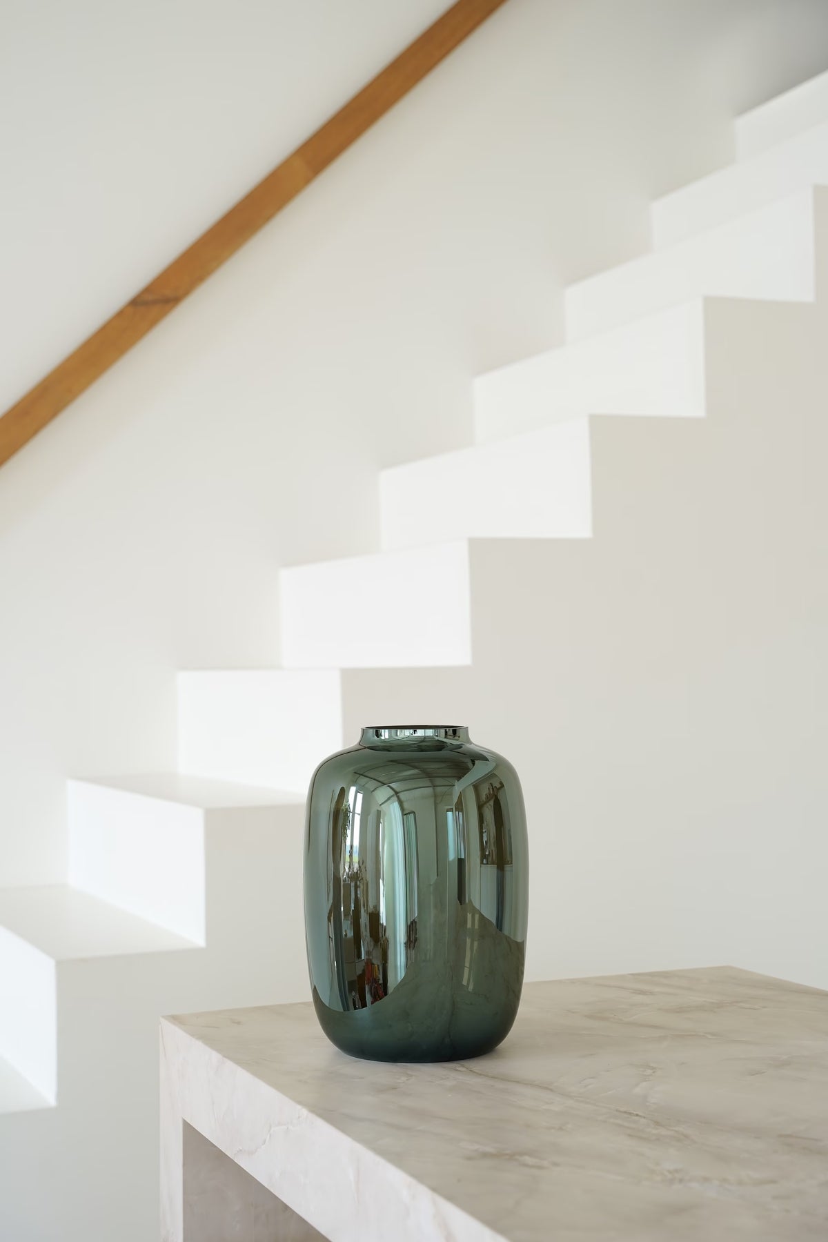 Vaas Glossy M met spiegelende glans op een lichte stenen sidetable naast een witte trap.