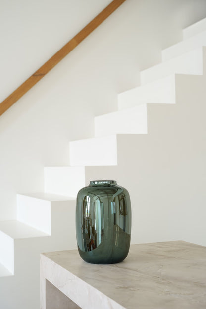 Vaas Glossy M met spiegelende glans op een lichte stenen sidetable naast een witte trap.