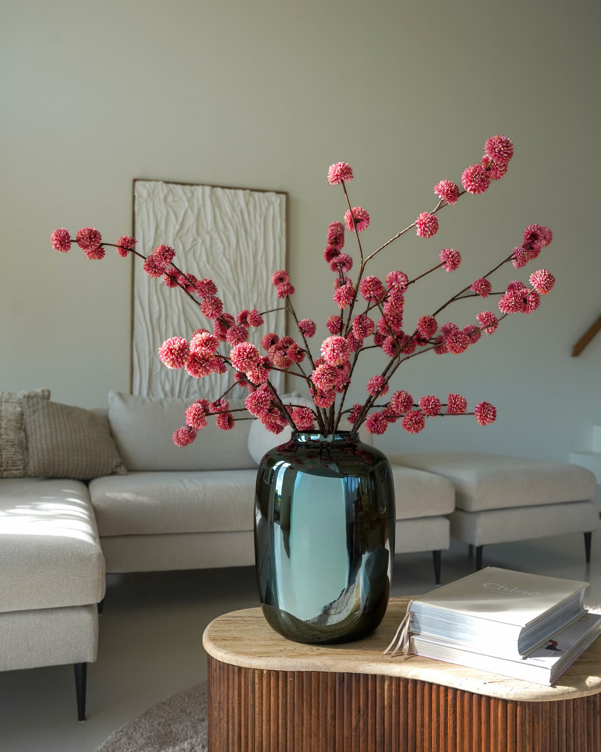Vaas Glossy M met roze zijden pompoms op een ronde houten salontafel in een lichte woonkamer.
