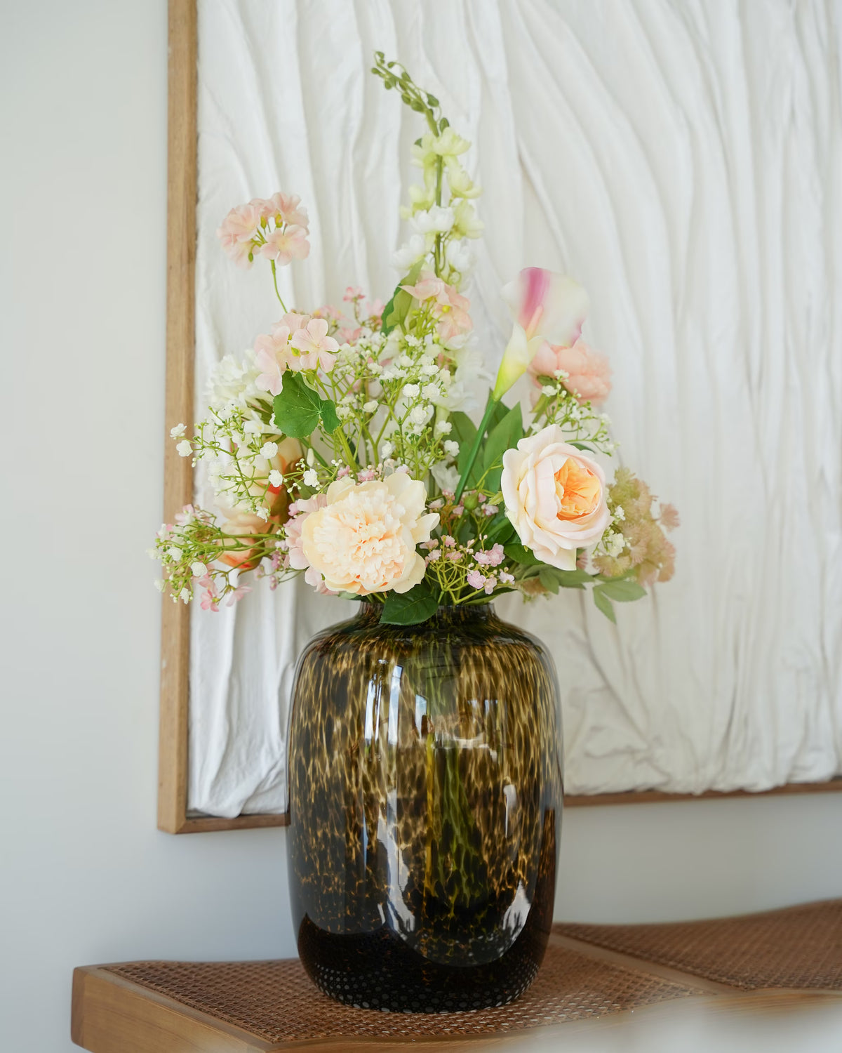 Glazen tijgervaas Leo M van Fan of Flowers met een zijden boeket in zachtroze, wit en crème op een houten bankje.