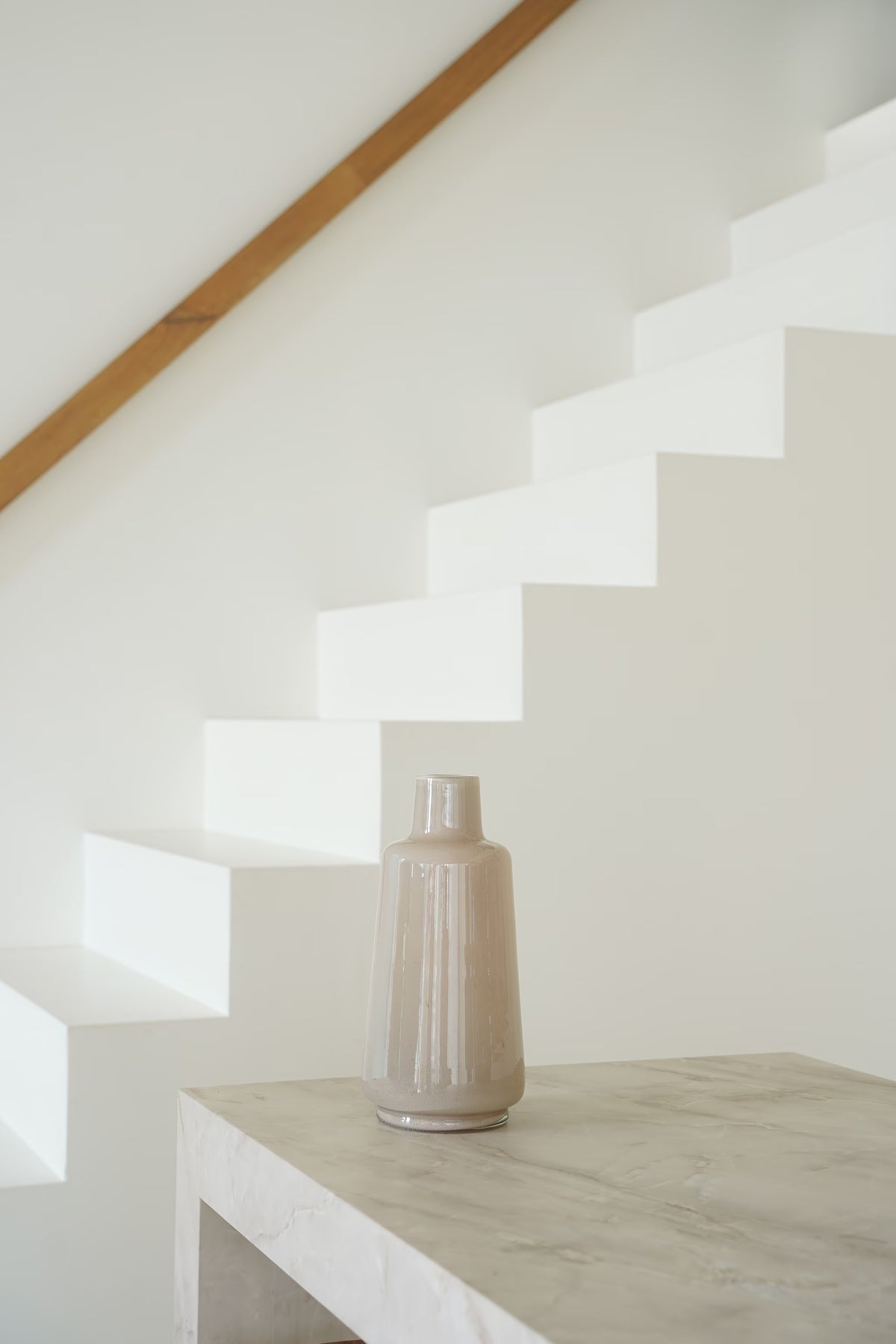 Beige Vaas Lino met glanzende afwerking en korte hals op een lichte stenen sidetable bij een witte trap.