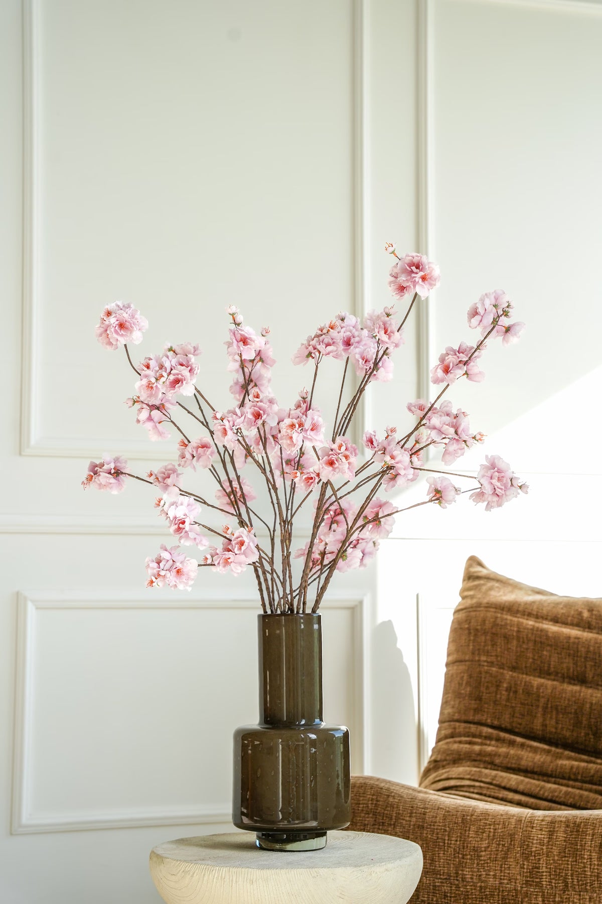 Vaas Madera met lichtroze zijden bloesems op een houten bijzettafel naast een bruine fauteuil.