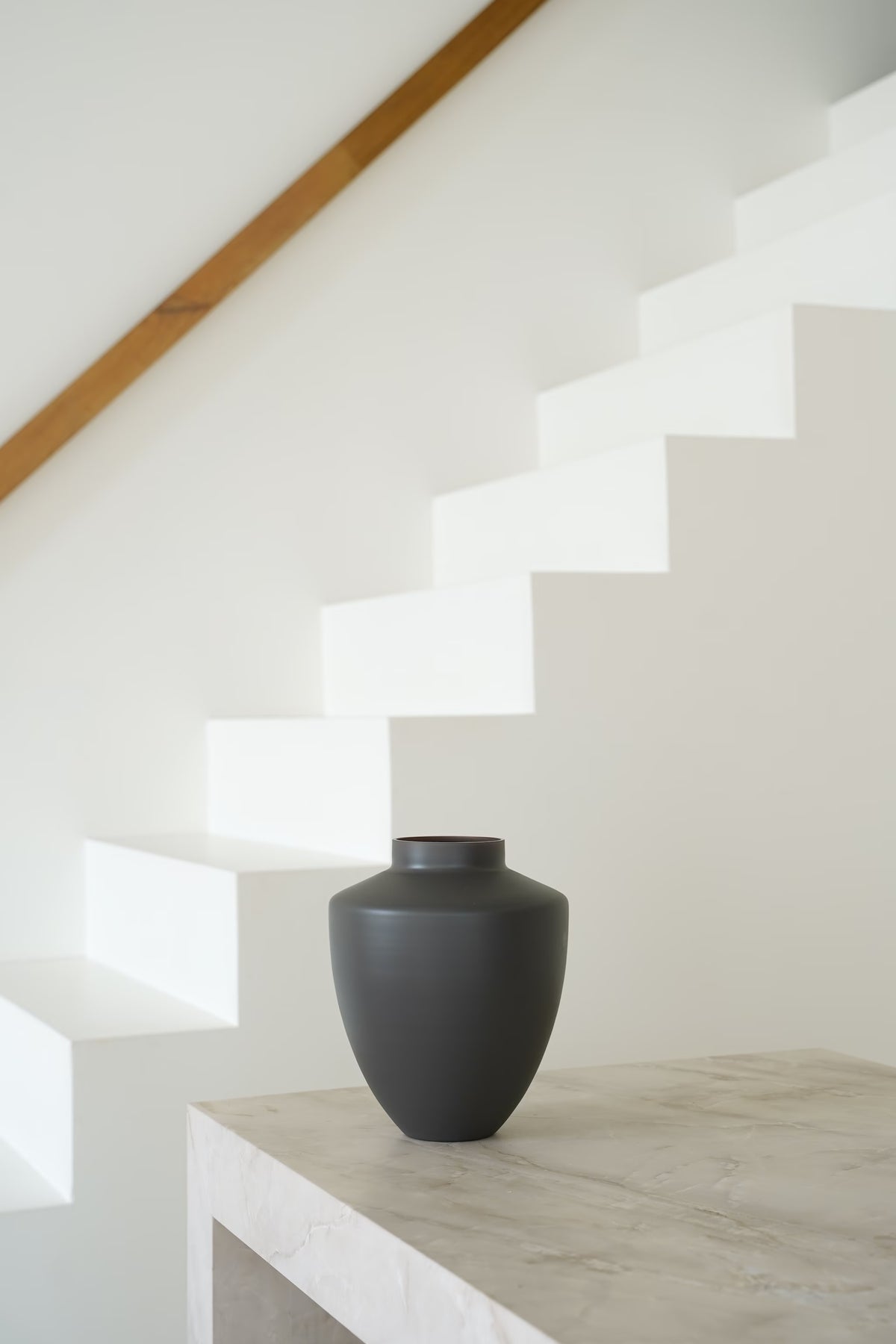 Matte grijsbruine Vaas Tierra S met brede schouders en korte hals op een lichte stenen sidetable.