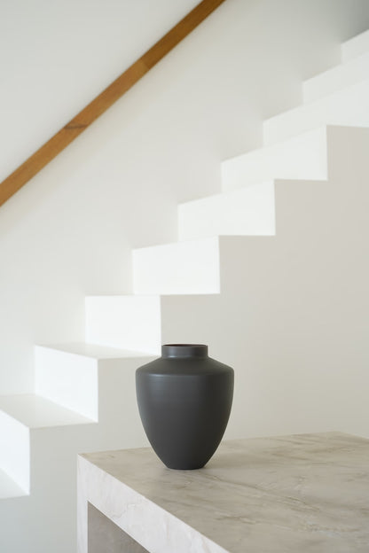 Matte grijsbruine Vaas Tierra S met brede schouders en korte hals op een lichte stenen sidetable.