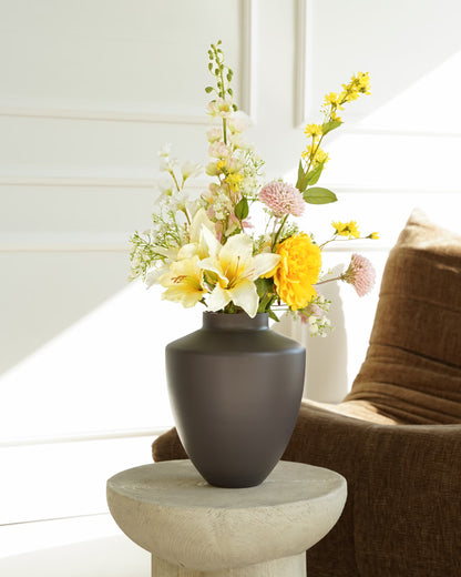 Vaas Tierra S met Zijden Boeket Mimosa in geel, wit en zachtroze op een houten bijzettafel naast een bruine fauteuil.