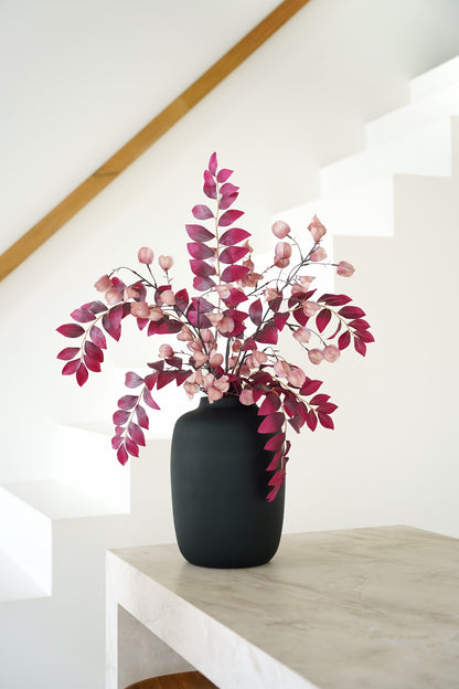 Zijden boeket Amaya van Fan of Flowers met bordeauxrode bladeren en roze lampionnetjes in matzwarte vaas Negro bij een witte trap.