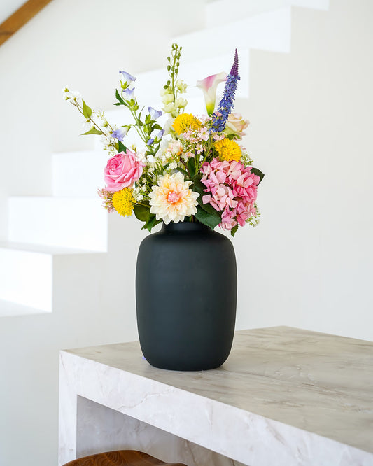Kleurrijk zijden boeket Bella van Fan of Flowers in matzwarte vaas Negro sfeervol gepresenteerd bij een trap.