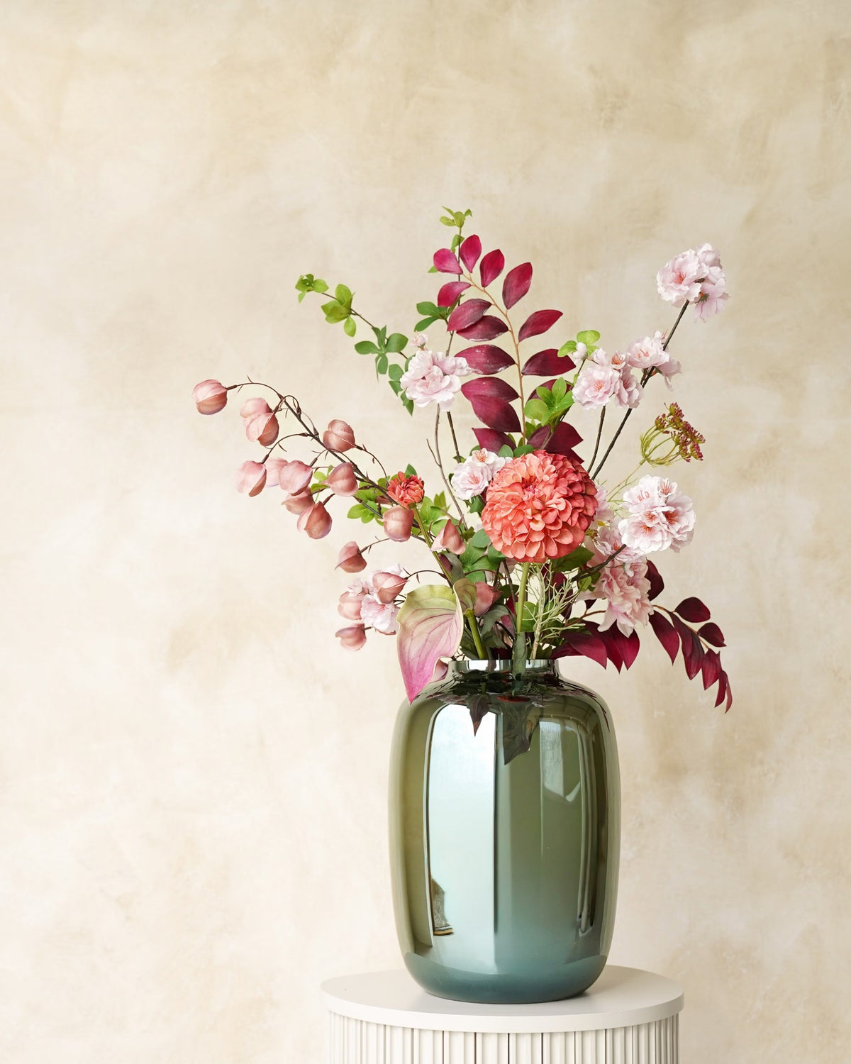 Zijden veldboeket Carmen van Fan of Flowers met roze bloesem, lampionnetjes en bordeauxrode bladeren in glanzende vaas Glossy op een ronde sokkel.
