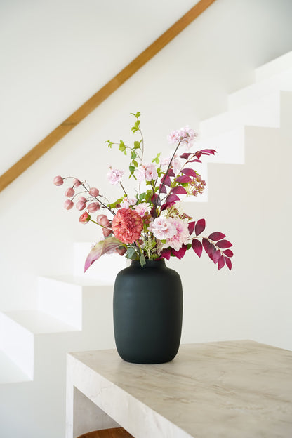 Zijden boeket Carmen van Fan of Flowers met roze bloemen, lampionnetjes en bordeauxrood blad in matzwarte vaas Negro bij een witte trap.