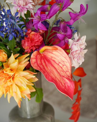 Detail van een koraalroze zijden anthurium met opvallende nerven, omringd door oranje, paarse en blauwe bloemen in boeket Chica van Fan of Flowers.