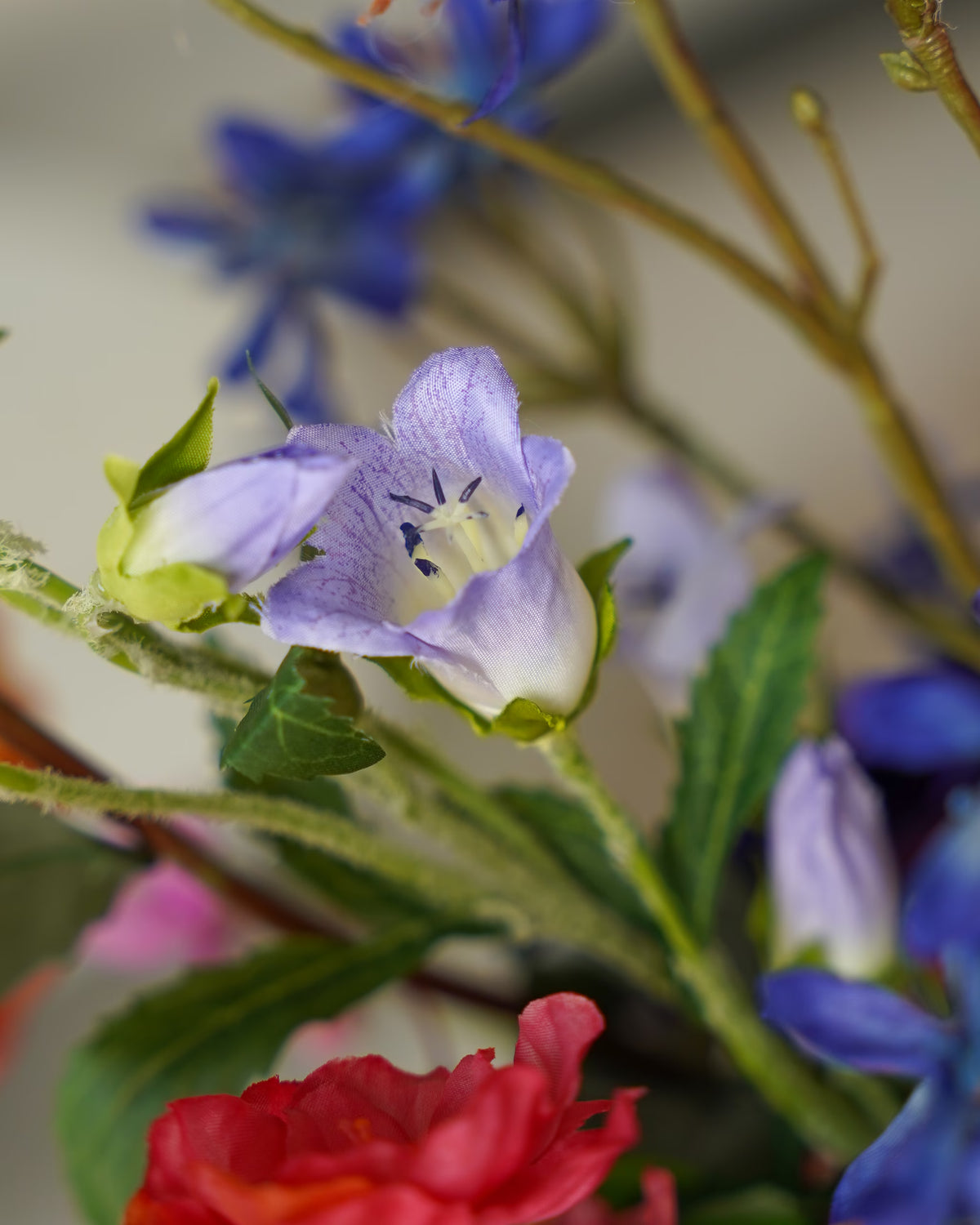 Detail van een lila zijden klokbloem tussen groen blad en blauwe en roze bloemen in boeket Chica van Fan of Flowers.