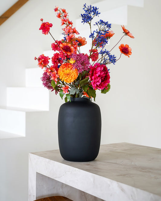 Zijden boeket Cielo van Fan of Flowers in matzwarte vaas op een marmeren dressoir bij een trap.