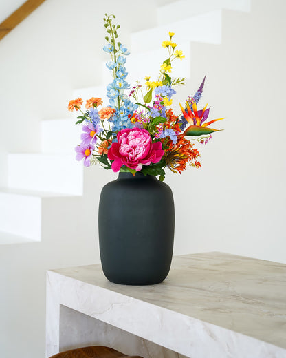 Kleurrijk zijden boeket Fiera van Fan of Flowers in matzwarte vaas Negro sfeervol gestyled bij een moderne trap.