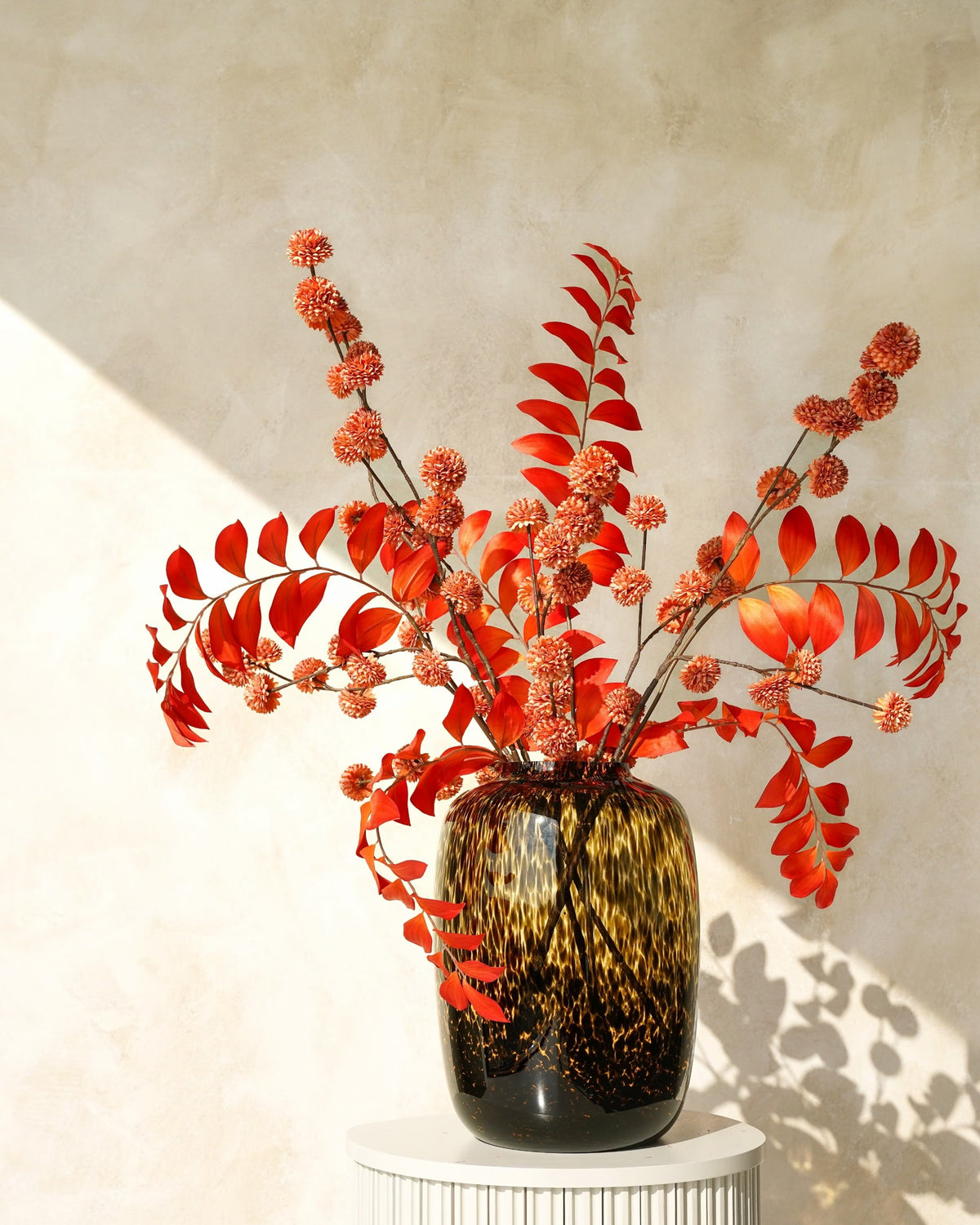Zijden herfstboeket Fuego van Fan of Flowers met oranje bladeren en roestkleurige bolbloemen in tijgervaas Leo op een ronde sokkel.