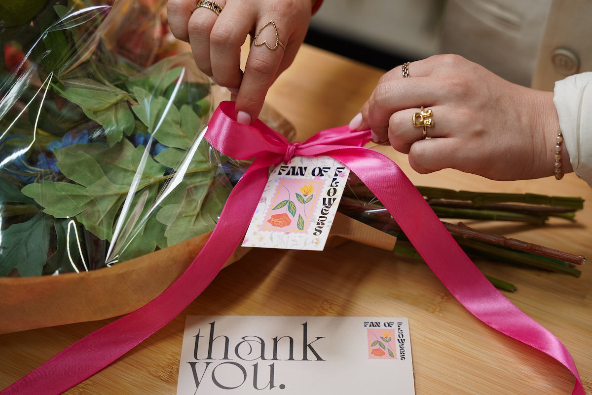 Femke pakt een zijden boeket in als het perfecte cadeau, inclusief een Fan of Flowers bedankkaartje en roze lint.
