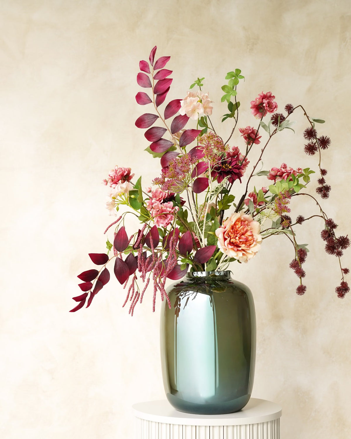 Zijden boeket Lila van Fan of Flowers met bordeauxrood blad, roze bloemen en zachte crèmetinten in glanzende vaas Glossy op een ronde sokkel.