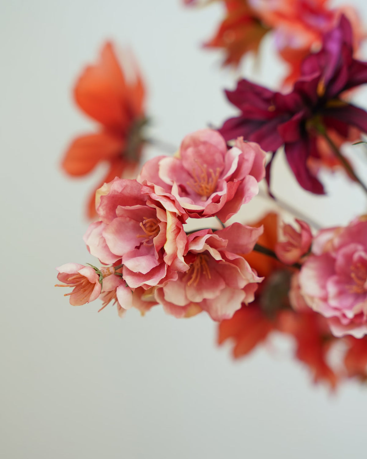 Detail van roze zijden bloemen met lichte bladranden in boeket Palma van Fan of Flowers, met bordeauxrode en oranje accenten op de achtergrond.
