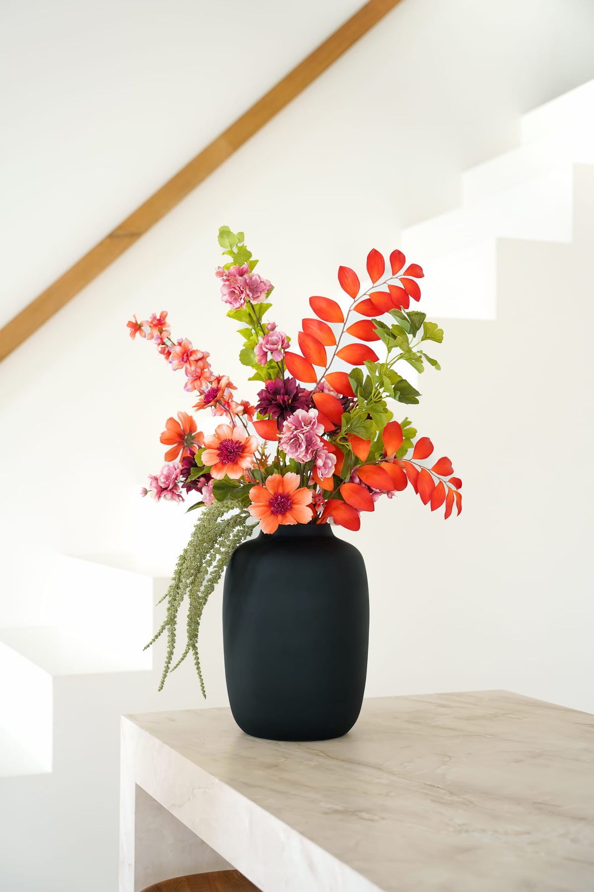 Zijden boeket Palma van Fan of Flowers met oranje en roze bloemen en groen blad in matzwarte vaas Negro bij een witte trap.