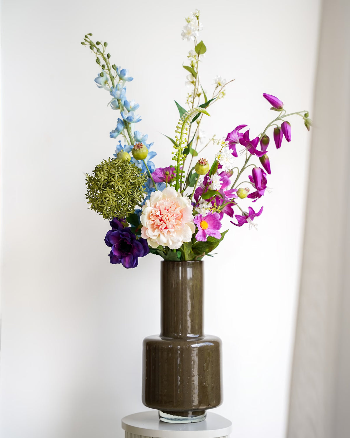 Zijden boeket Rio van Fan of Flowers met lichtblauwe, paarse en crèmekleurige bloemen in een bruine glazen vaas met lange hals.