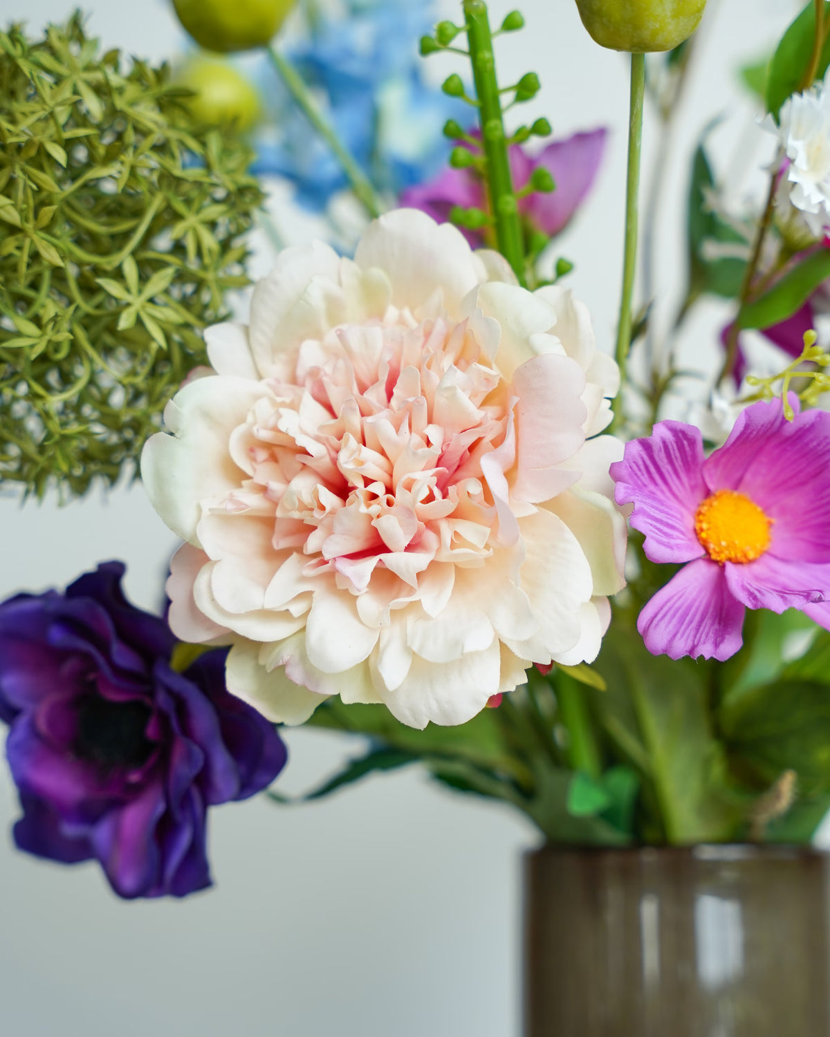 Detail van een crèmekleurige zijden bloem met zachtroze hart, omringd door paarse bloemen en groene accenten in boeket Rio van Fan of Flowers.