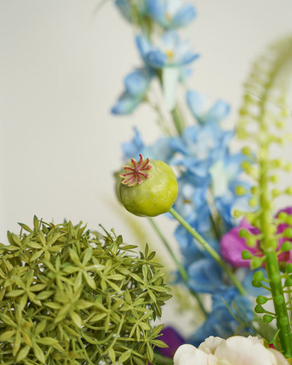 Detail van een groene zaaddoos naast een groene bolbloem en lichtblauwe bloemen in zijden boeket Rio van Fan of Flowers.