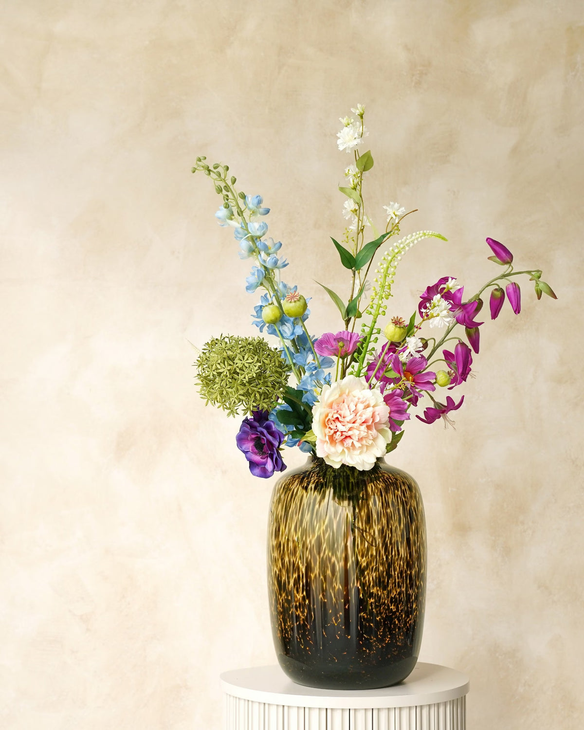 Zijden boeket Rio van Fan of Flowers met lichtblauwe en paarse bloemen, een crèmekleurige bloem en frisgroen in tijgervaas Leo op een ronde sokkel.