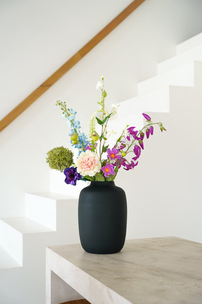 Zijden boeket Rio van Fan of Flowers met lichtblauwe, paarse en crèmekleurige bloemen in matzwarte vaas Negro bij een witte trap.