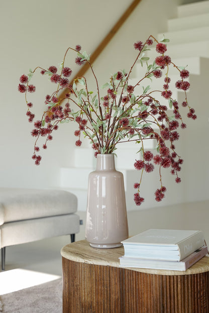 Bruine zijden bolletjestakken van Fan of Flowers met sierlijk afhangende vertakkingen in een slanke lichtbeige vaas op een ronde bijzettafel.