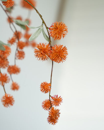 Detail van oranje decoratieve bolletjes en grijsgroene blaadjes aan een sierlijk gebogen zijden tak van Fan of Flowers.