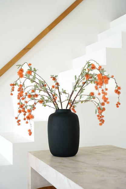 Oranje zijden bolletjestakken van Fan of Flowers met grijsgroene blaadjes in matzwarte vaas Negro bij een witte trap.